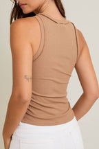 Woman wearing a beige sleeveless top against a plain background