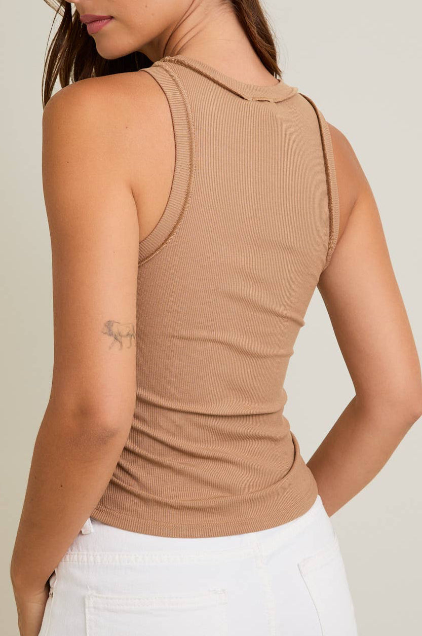 Woman wearing a beige sleeveless top against a plain background