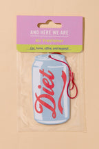 A Diet air freshener car fragrance shaped like a light blue soda can with red script lettering, sealed in a clear plastic bag with a pink and green header card that reads 'AND HERE WE ARE Diet freshener'.