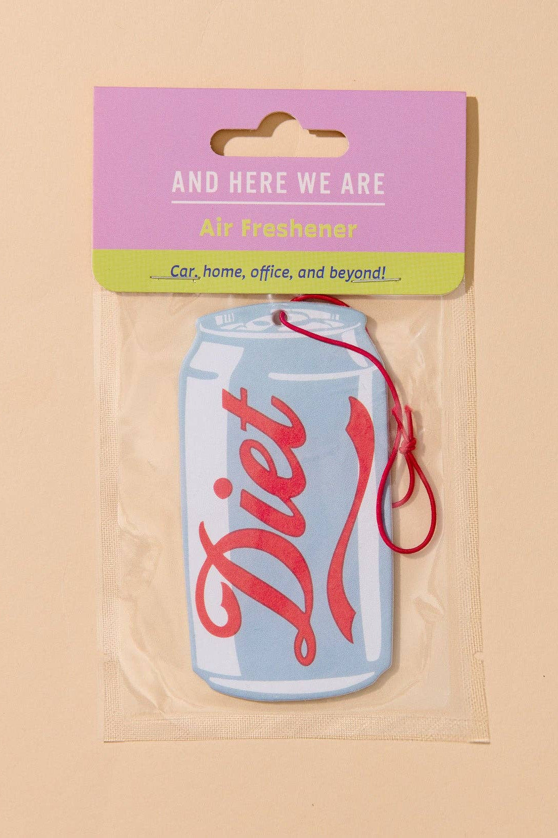 A Diet air freshener car fragrance shaped like a light blue soda can with red script lettering, sealed in a clear plastic bag with a pink and green header card that reads 'AND HERE WE ARE Diet freshener'.
