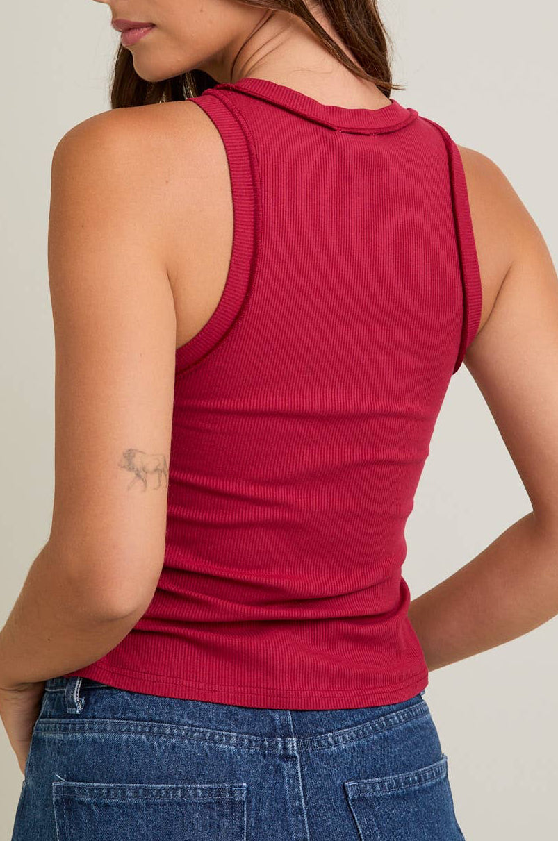 Person wearing a red sleeveless top and blue jeans on a plain background