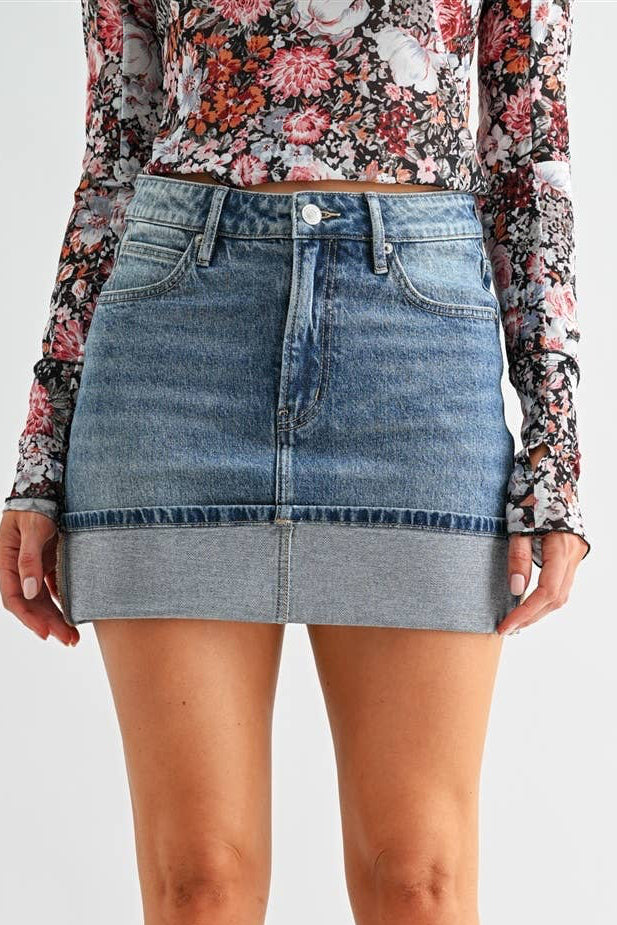 Person wearing a floral top, denim skirt, and black knee-high boots on a light gray background