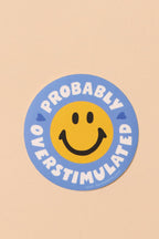 Circular sticker with smiley face and text 'Probably Overstimulated' on a beige background