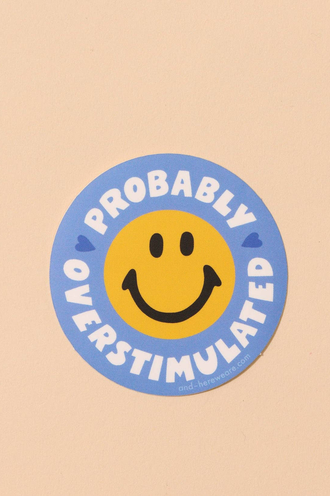 Circular sticker with smiley face and text 'Probably Overstimulated' on a beige background