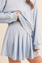 Woman wearing a light blue sweater and skirt set on a beige background