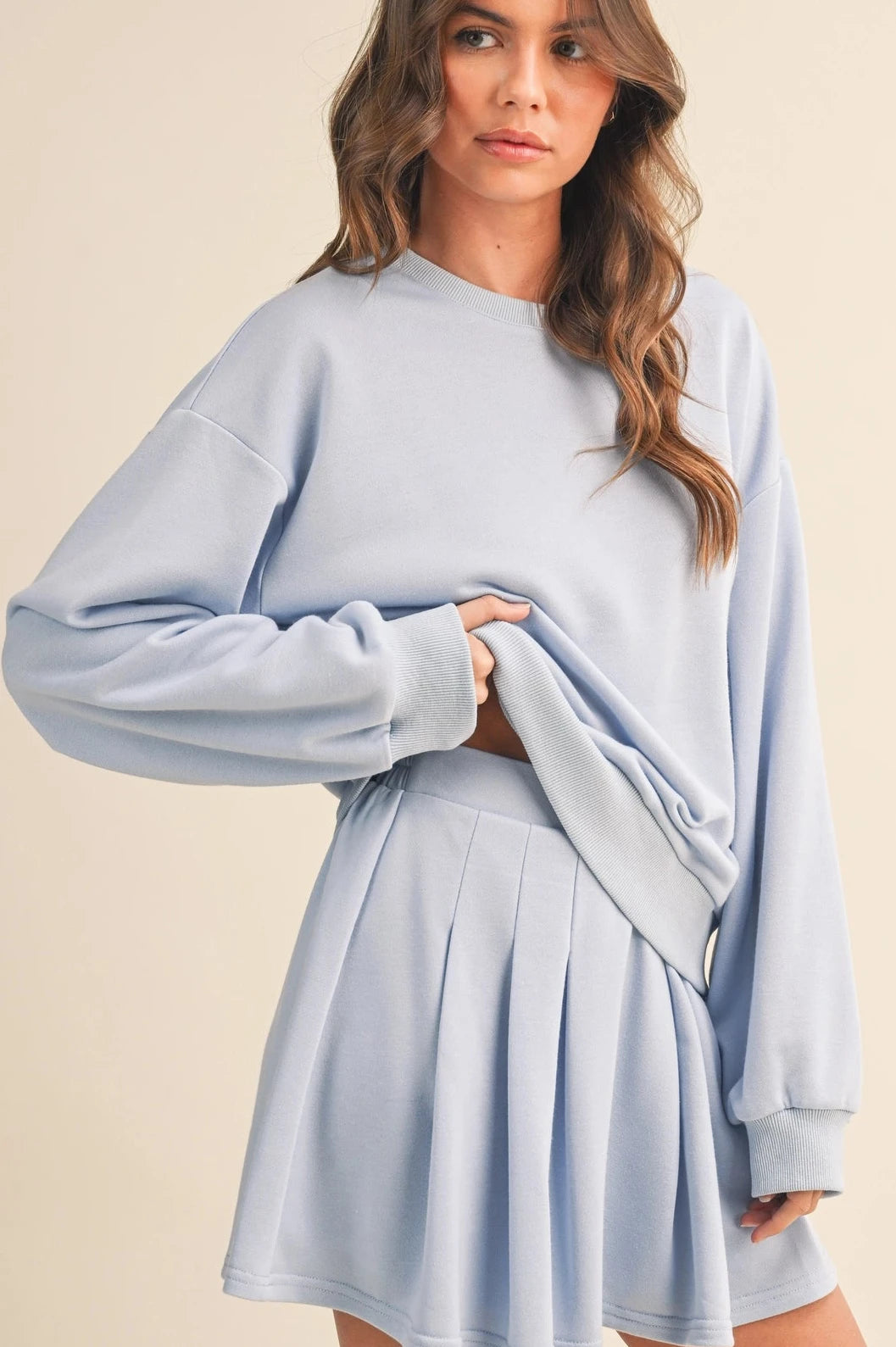 Woman wearing a light blue sweater and skirt set on a beige background