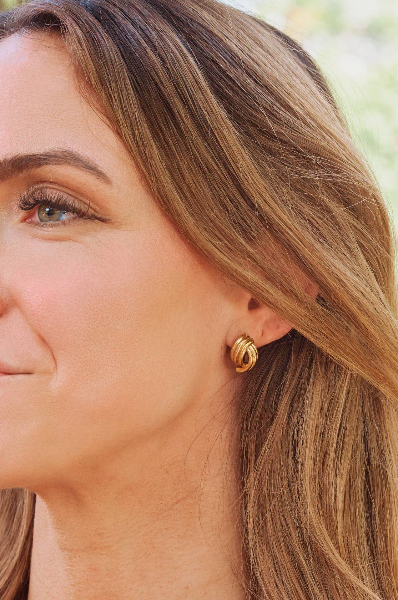 Woman wearing gold hoop earrings with a blurred natural background