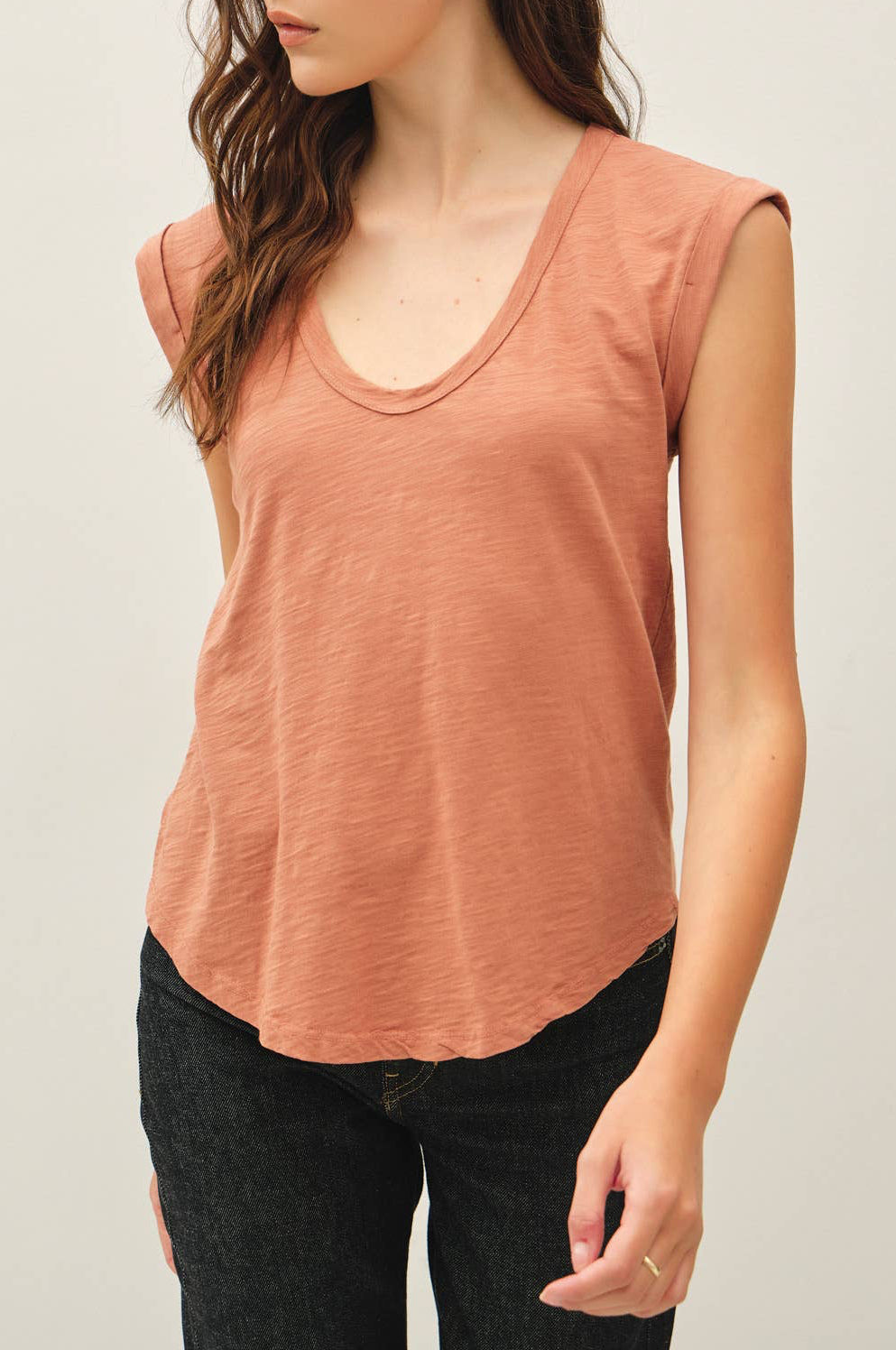 Woman wearing a sleeveless rust-colored top against a plain background
