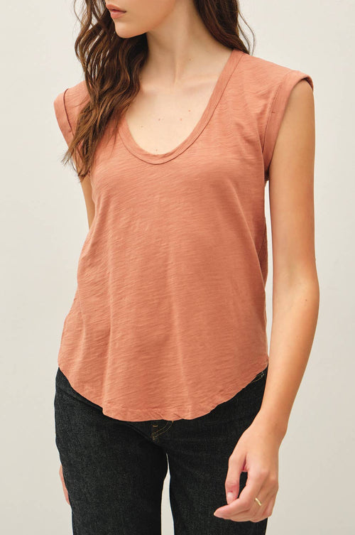 Woman wearing a sleeveless rust-colored top against a plain background