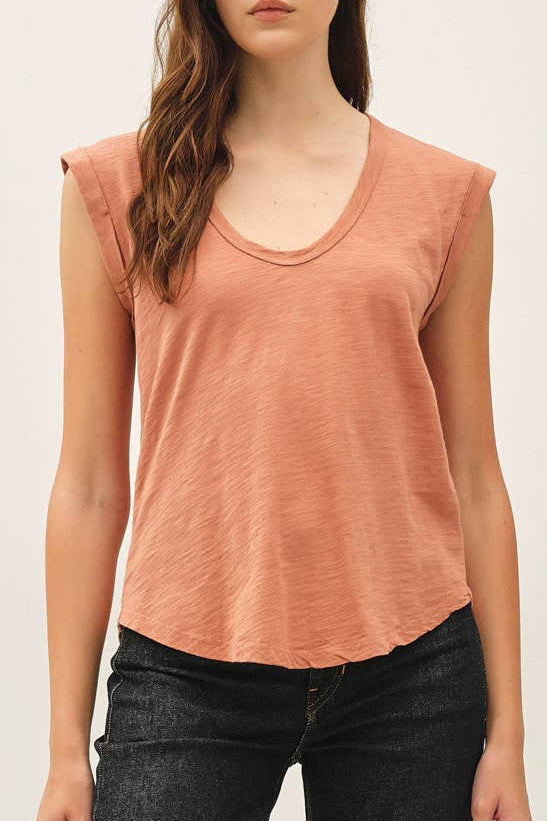 Woman wearing a peach tank top and black jeans against a white background