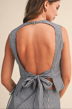 Woman wearing a gray striped top with an open back and bow detail on a beige background