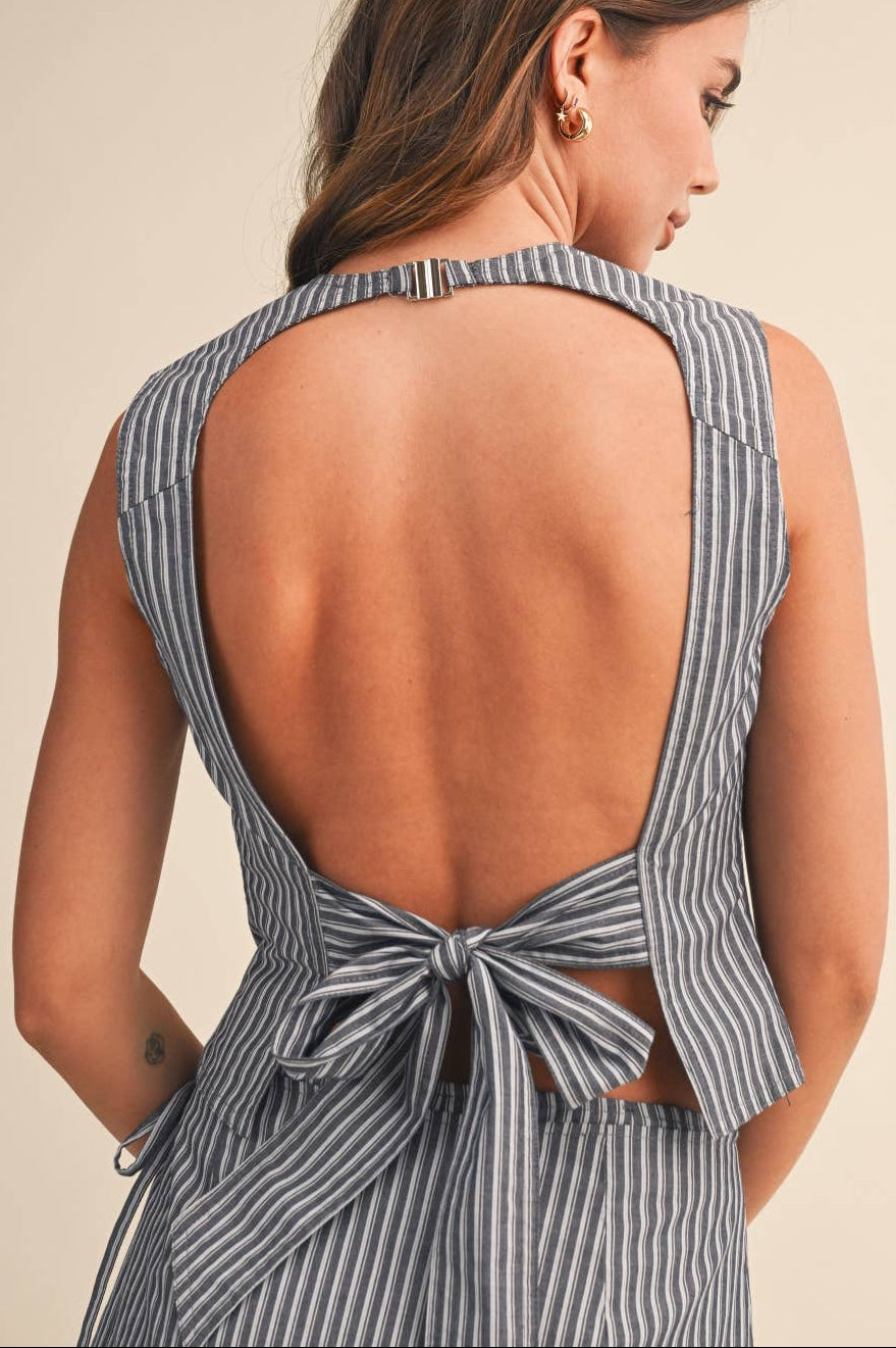 Woman wearing a gray striped top with an open back and bow detail on a beige background