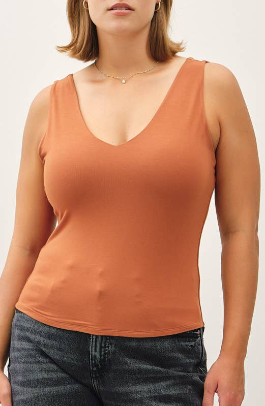 Woman wearing a rust-colored tank top and dark jeans against a white background