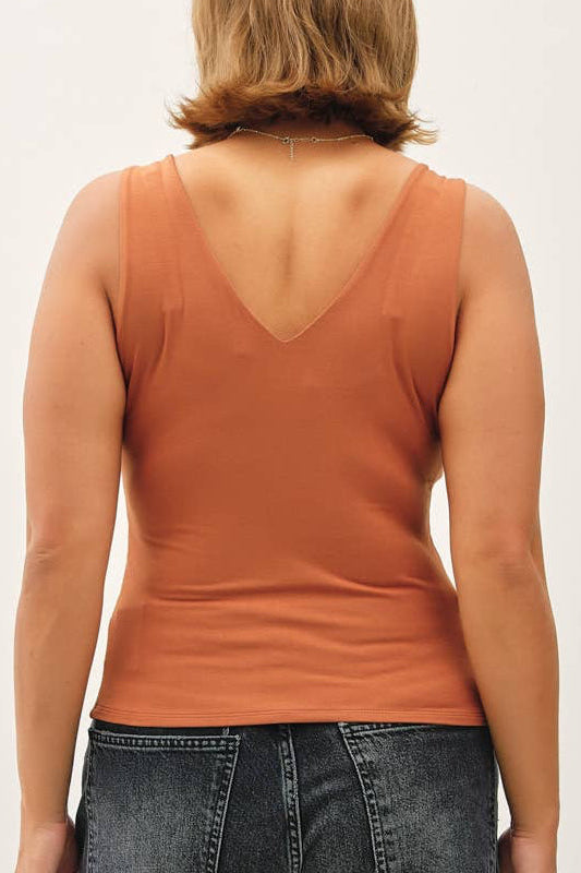 Person wearing a rust-colored tank top and dark jeans on a white background