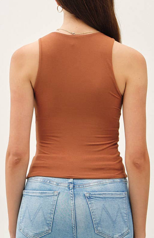 Woman wearing a brown tank top and light blue jeans against a white background