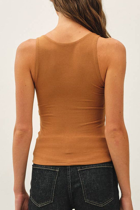 A woman shown from the back wearing a fitted sleeveless rust-orange top and dark blue flare jeans, standing against a plain white studio background.