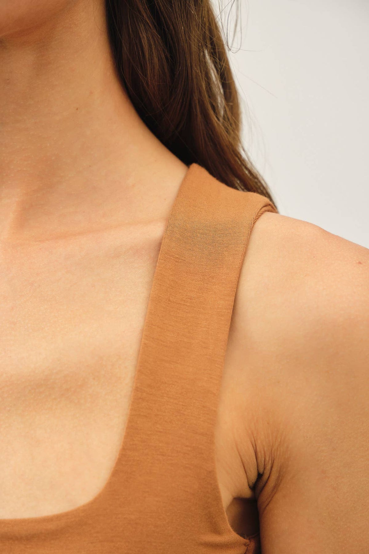 Close-up of a model wearing a scoop-neck tank top in a warm camel brown color, showing the shoulder strap and upper chest area.