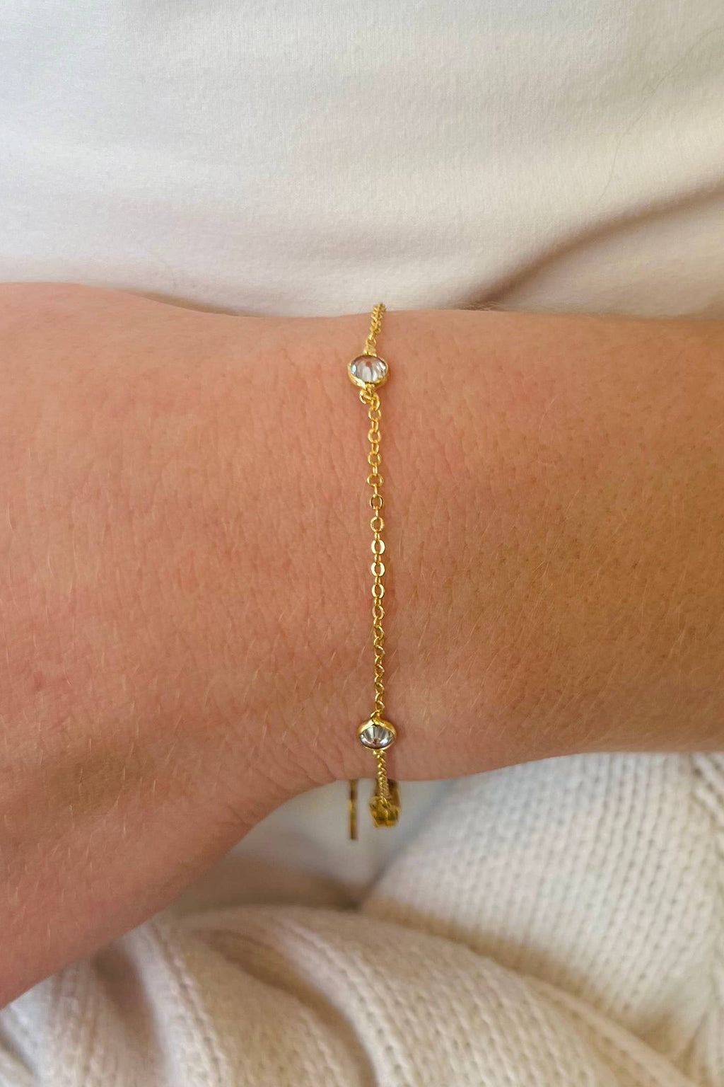 Gold bracelet with cubic zirconia on a wrist against a white background