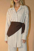 Woman wearing a striped shirt and wide-leg pants with a brown belt against a beige background