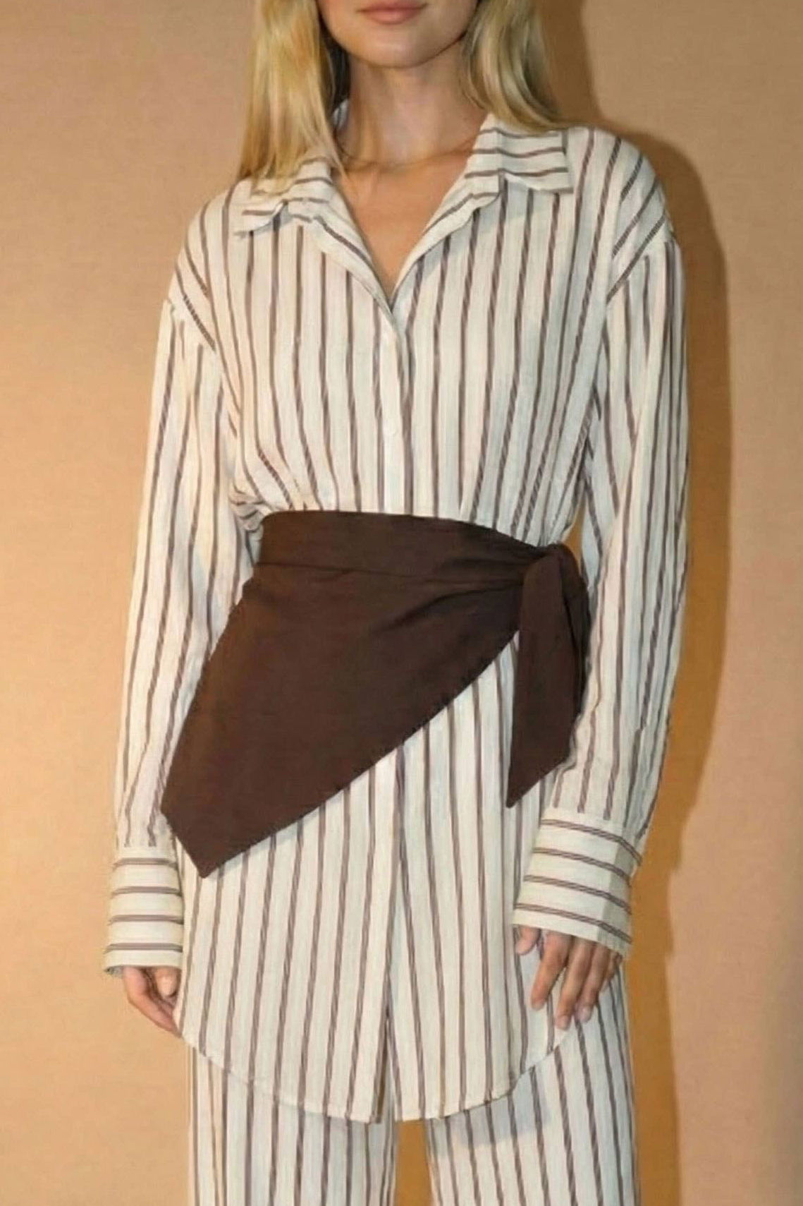 Woman wearing a striped shirt and wide-leg pants with a brown belt against a beige background