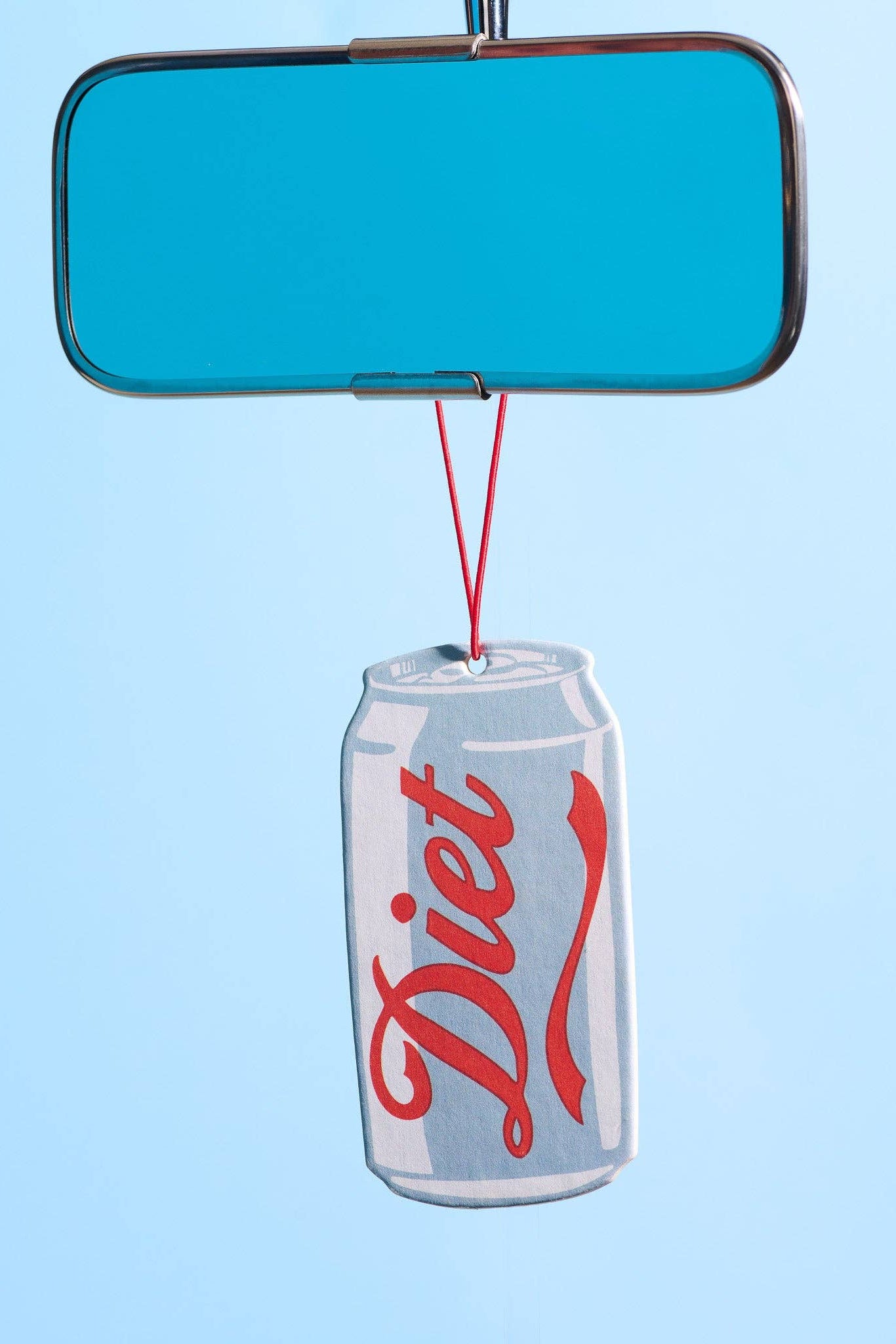A novelty car rearview mirror ornament featuring a silver aluminum Diet Coke can with the red script logo, hanging from a blue mirror by a red string against a light blue background.