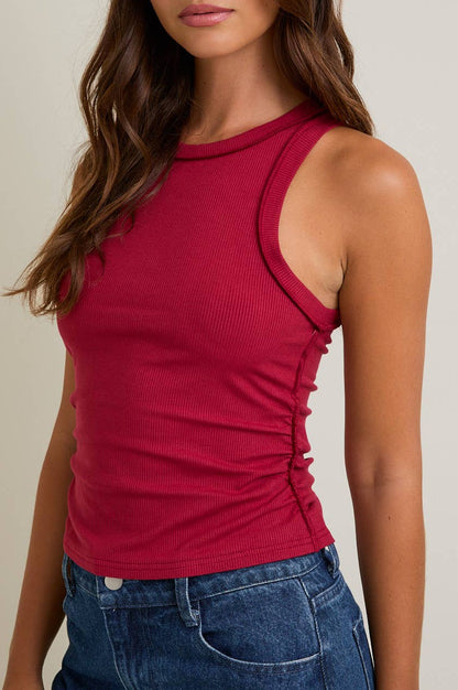 Red sleeveless top with ruched detail worn by a person on a neutral background