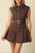 A woman modeling a sleeveless brown mini dress with a pointed collar, button front, and matching belt with a square buckle, set against a plain beige background.