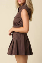 A woman modeling a sleeveless brown mini dress with a pleated skirt, shown in profile against a plain beige studio background.