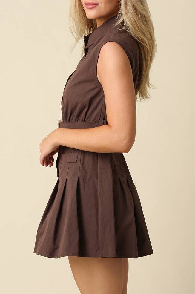 A woman modeling a sleeveless brown mini dress with a pleated skirt, shown in profile against a plain beige studio background.