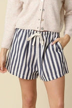 Woman wearing a white shirt and striped shorts on a beige background