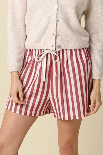 Woman wearing a white button-up shirt and red and white striped shorts on a beige background