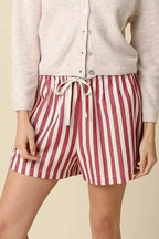 Woman wearing a white button-up shirt and red and white striped shorts on a beige background