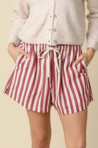 Woman wearing a white cardigan and red and white striped shorts on a beige background