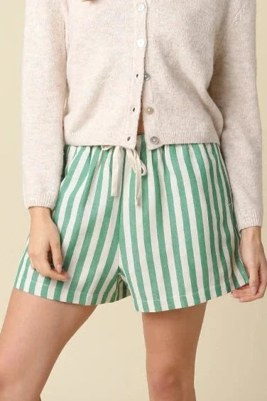 Woman wearing a white button-up shirt and green striped shorts on a beige background