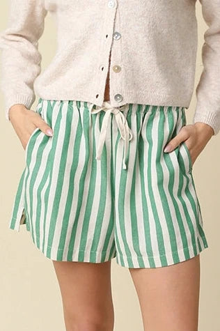 Woman wearing a white cardigan and green striped shorts on a beige background