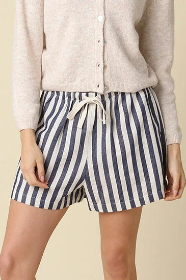 Woman wearing a light-colored cardigan and striped shorts on a beige background