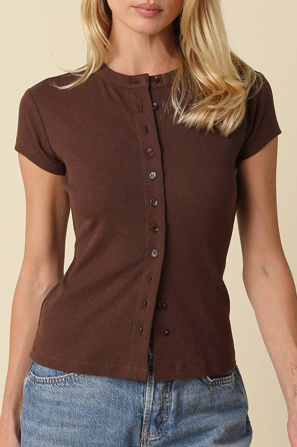 Woman wearing a brown short-sleeve button-up shirt and blue jeans on a beige background