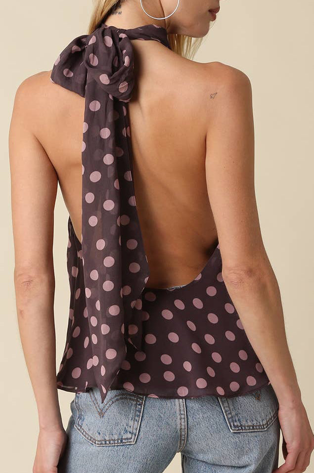 Woman wearing a polka dot top with an open back and light blue jeans on a beige background