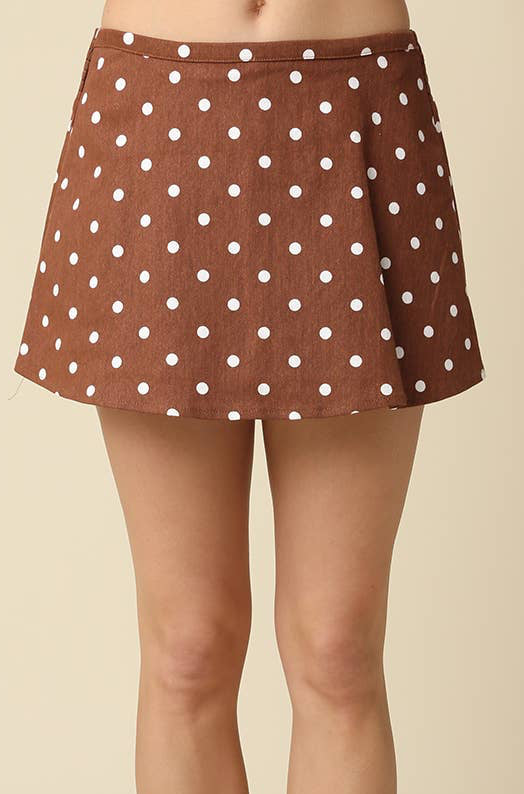 A person wearing a brown mini skirt with white polka dots, white socks, and brown sneakers with gold stripes, shown from the waist down against a plain beige background.