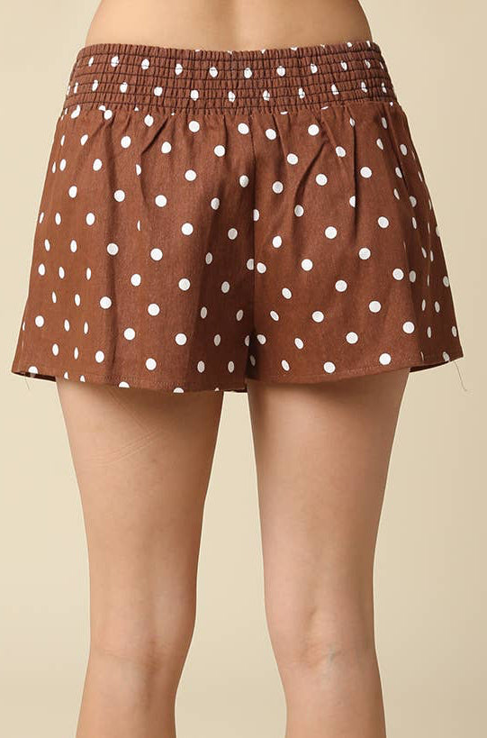 Brown shorts with white polka dots, modeled from the back against a solid beige background.