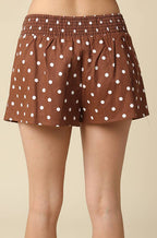 Brown shorts with white polka dots, modeled from the back against a solid beige background.