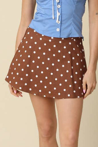 A woman modeling a two-piece outfit consisting of a light blue strapless corset-style top and a brown mini skirt with white polka dots, paired with brown shoes and white socks, against a solid beige background.