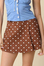 A woman modeling a light blue strapless top paired with a brown mini skirt featuring white polka dots, styled with white socks and brown sneakers against a solid beige background.