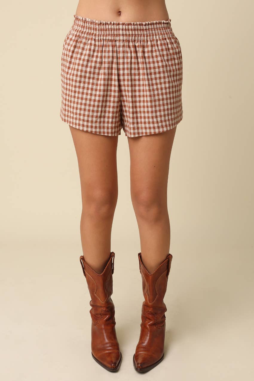 Person wearing red and white checkered shorts with brown leather boots on a beige background