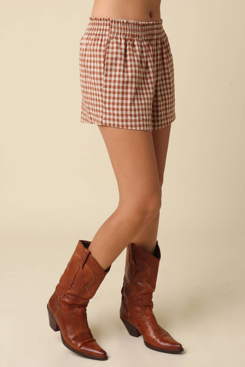 Person wearing a checkered skirt and brown cowboy boots on a beige background