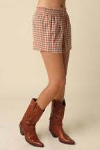 Person wearing a checkered skirt and brown cowboy boots on a beige background