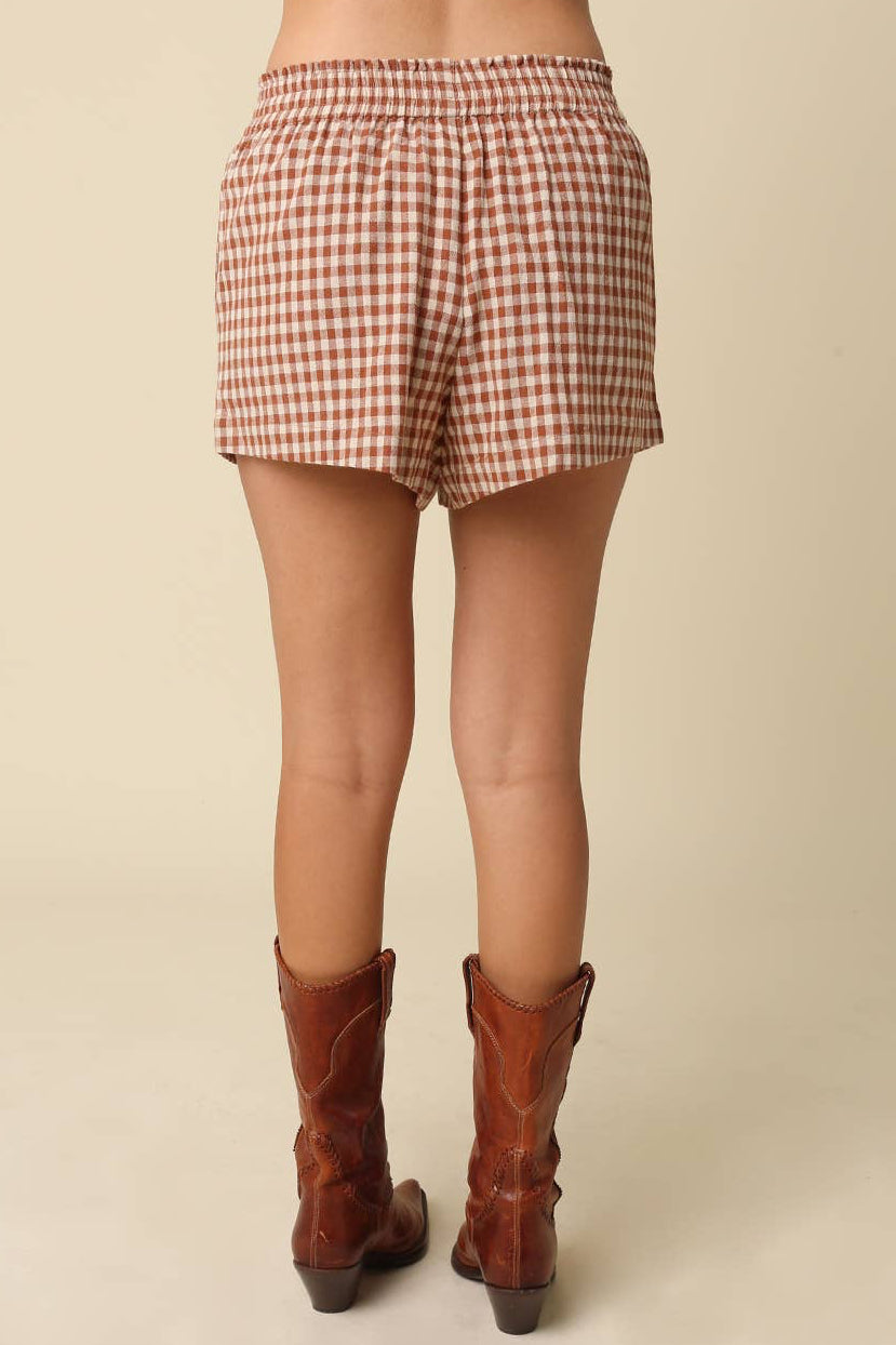 Person wearing red and white checkered shorts and brown cowboy boots on a beige background