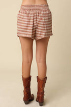 Person wearing red and white checkered shorts and brown cowboy boots on a beige background