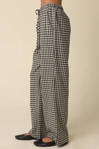 Black and white gingham wide-leg pants with an elastic drawstring waist, shown on a model from the waist down wearing black flats against a solid beige background.