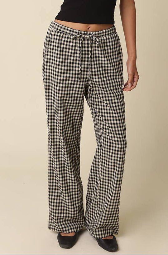 Person wearing a black tank top and checkered pants on a beige background